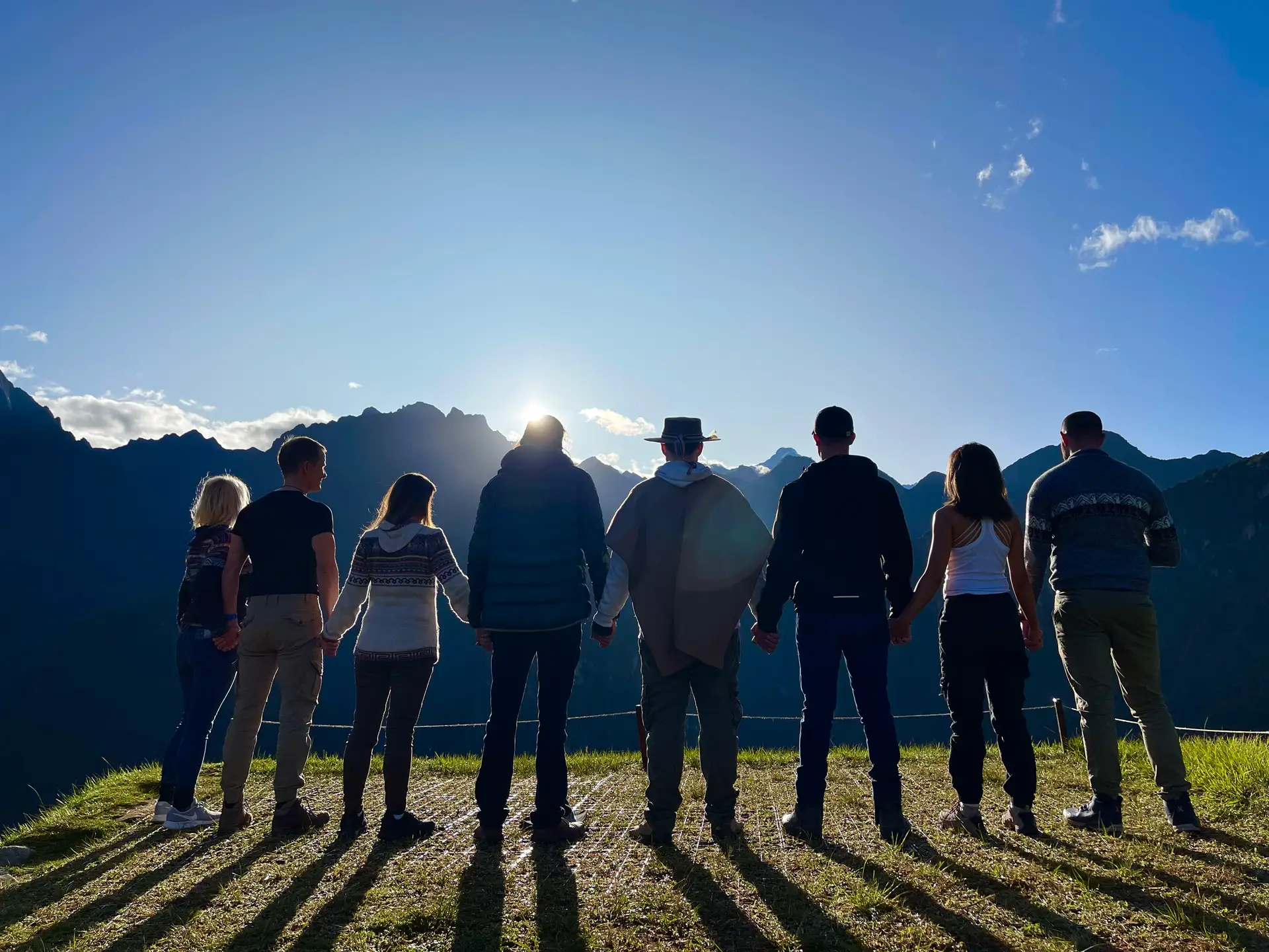 A small group holding hands at Machu Picchu as the sun crests the mountains