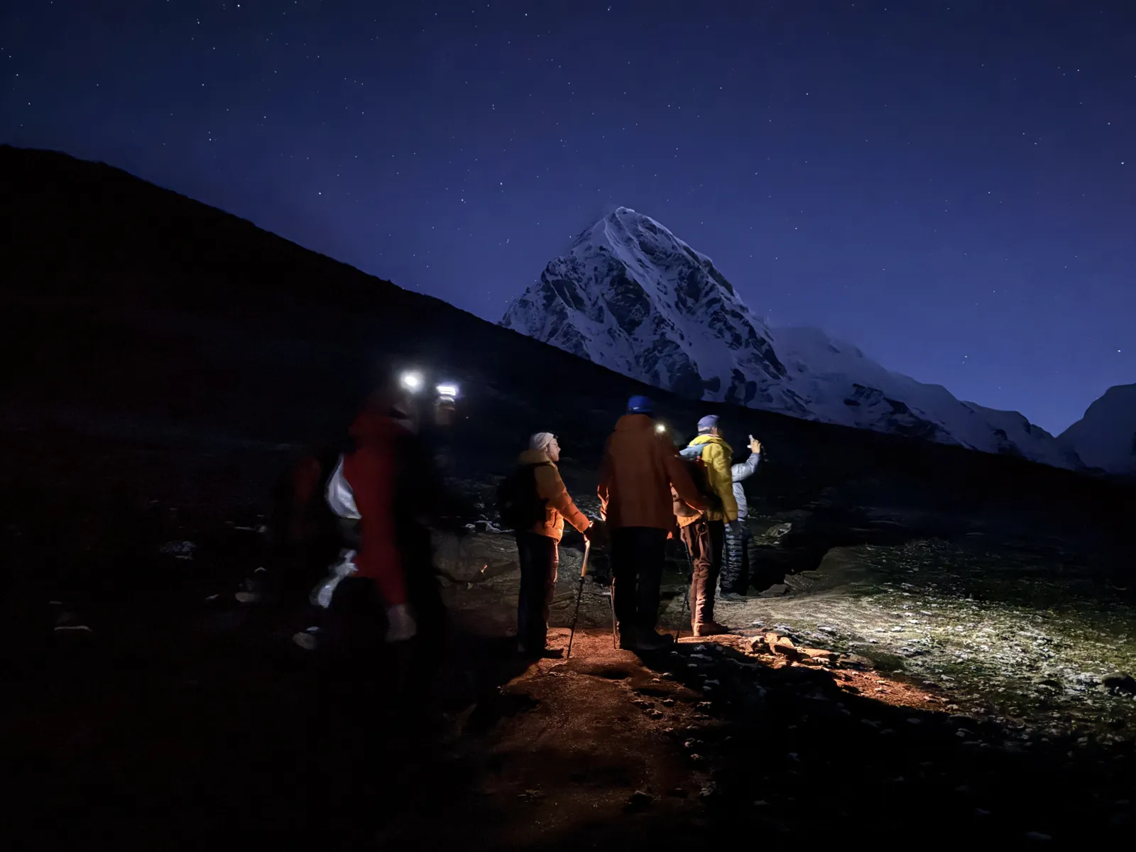 Trekkers with headlamps climbing toward Kala Patthar before dawn under the stars