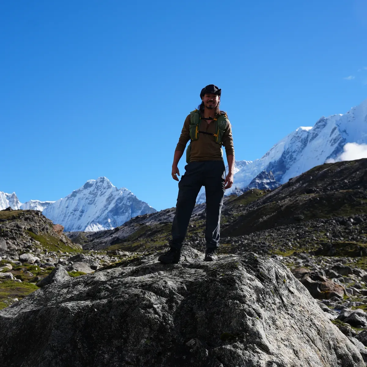 Lane Belone standing on a boulder below snow peaks in the Khumbu, Nepal